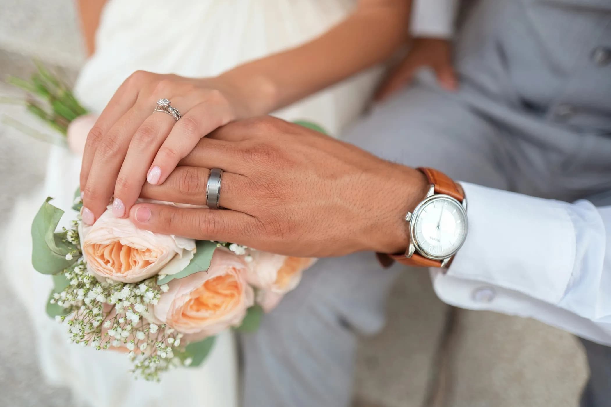 Mani di due sposi che si toccano sul bouquet di rose durante la cerimonia civile di matrimonio, fedi nuziali visibili — il momento della firma del registro accompagnato dalla musica dal vivo